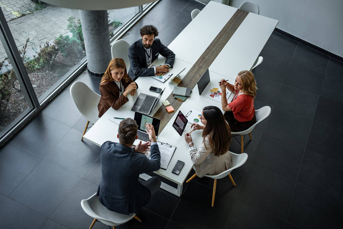 Aerial view of four people in business attire having a meeting around a conference table with laptops.