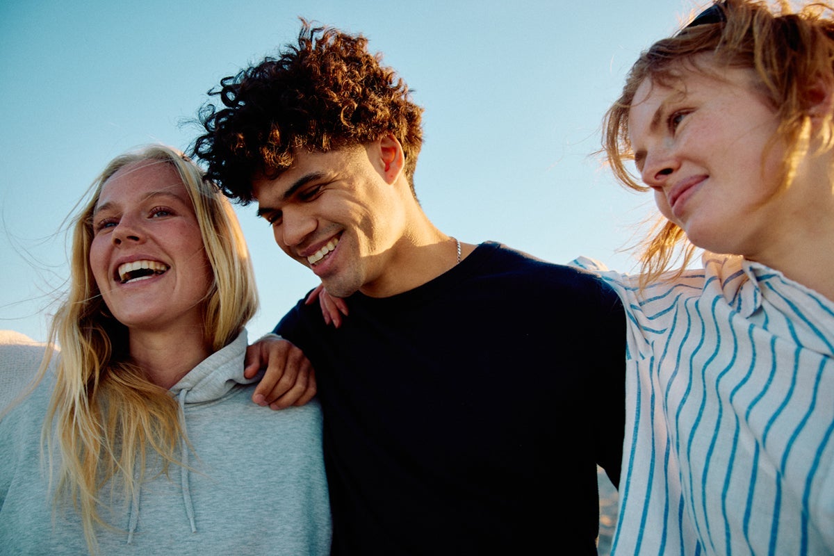 Three friends smiling with arms around each other outdoors under a clear blue sky.
